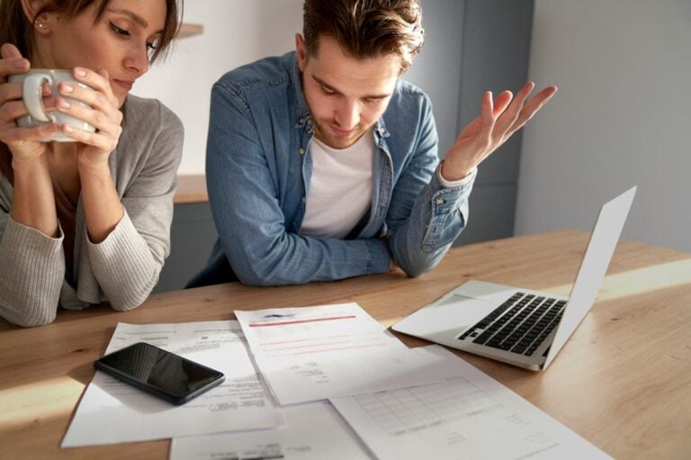 Worried couple sitting at a kitchen table reviewing bills and a laptop after a job loss, thinking through their mortgage options