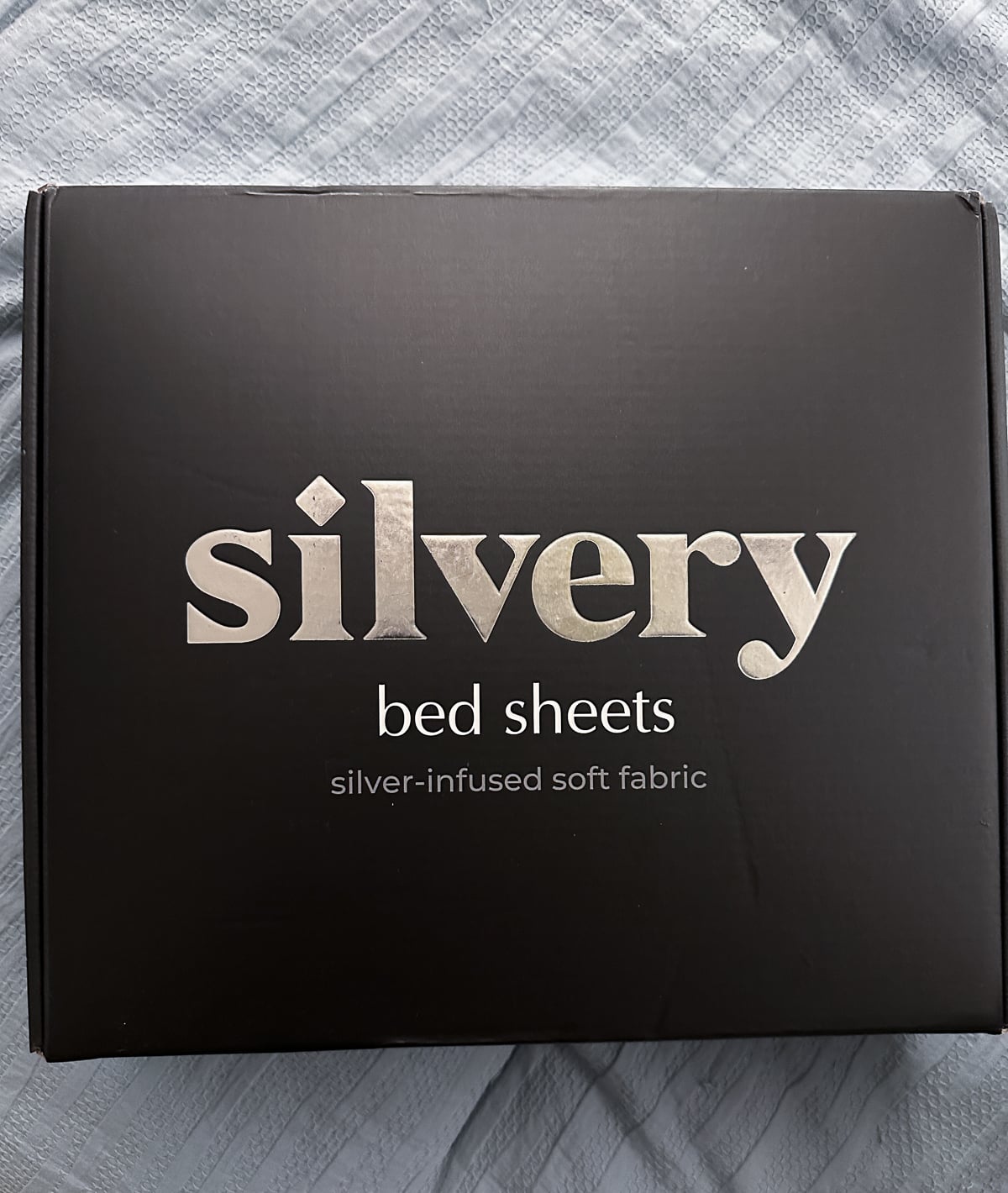 Closed black Silvery bed sheets box with a silver foil logo resting on the bed