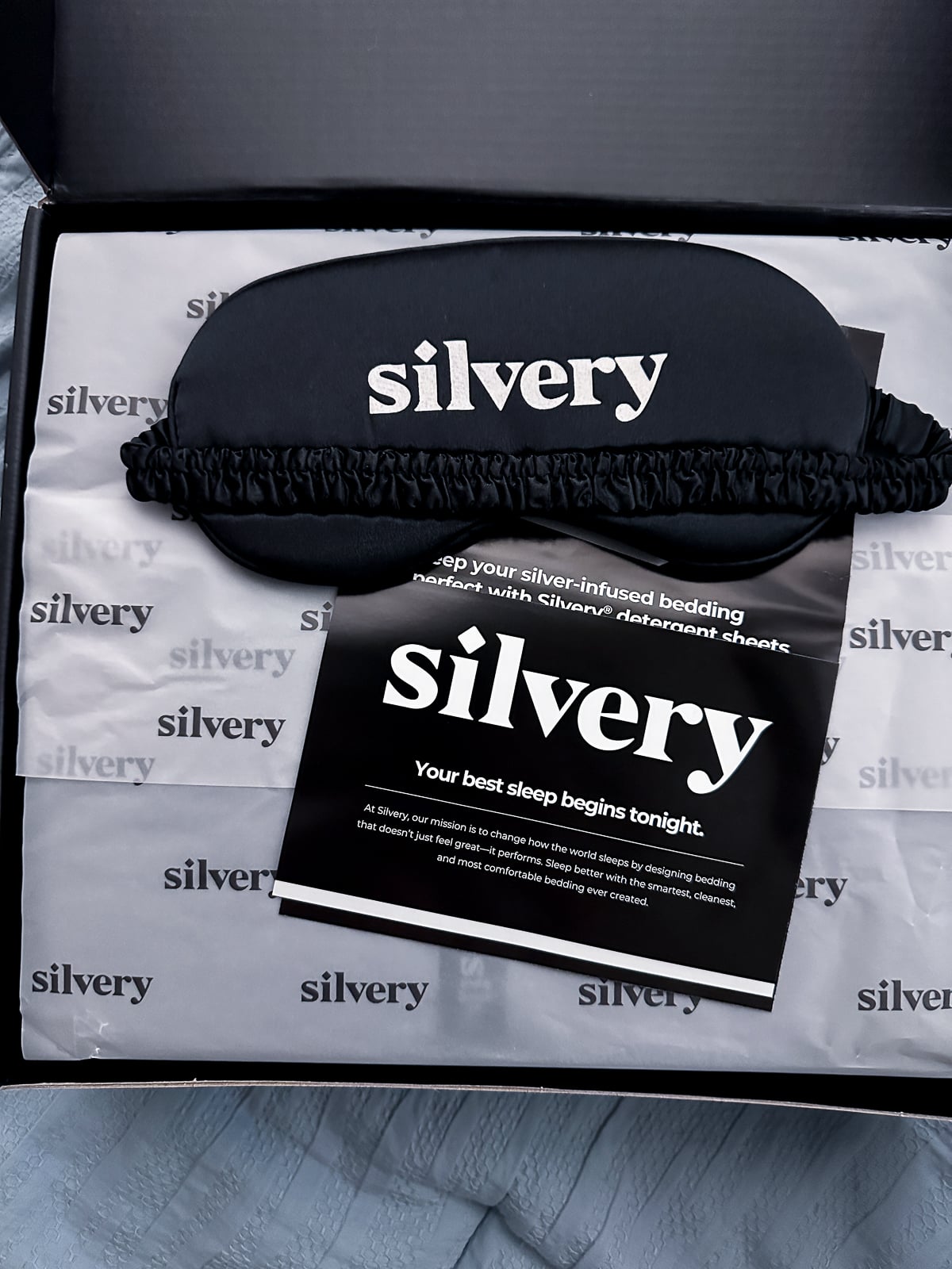 Open Silvery box with a black satin sleep mask and a card that reads your best sleep begins tonight