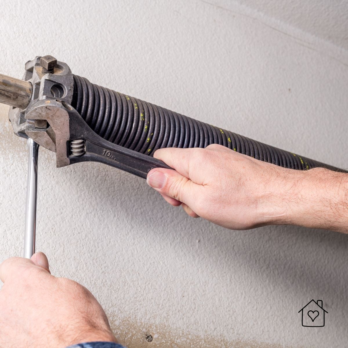 Hands using a wrench to adjust a garage door torsion spring during installation