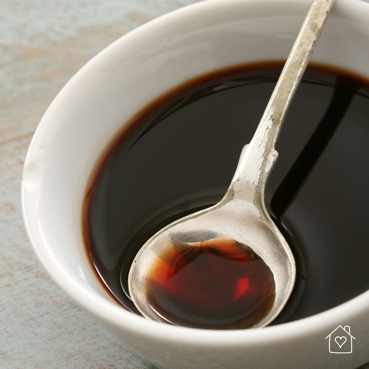 Thin balsamic vinegar in a white bowl with an antique silver spoon, before it's reduced into a thick glaze