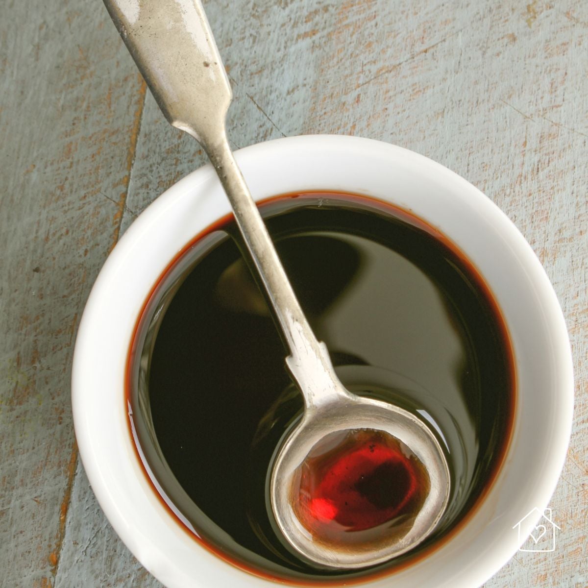 Overhead view of balsamic vinegar in a white bowl with a vintage spoon resting inside