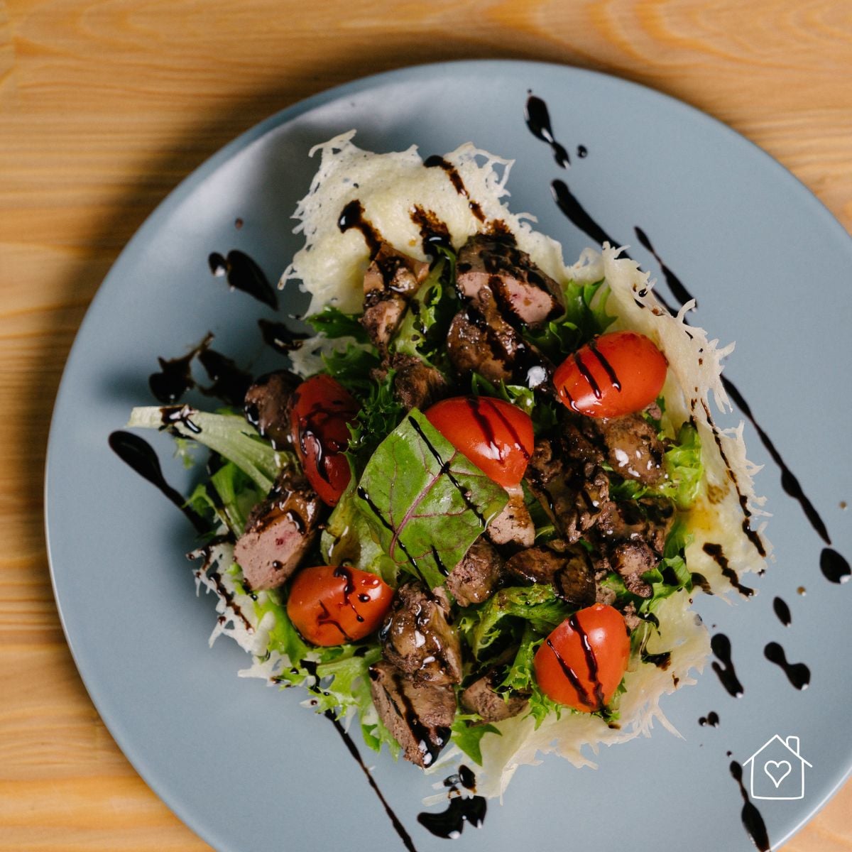 Salad with cherry tomatoes and a parmesan crisp on a gray plate, finished with a balsamic glaze drizzle