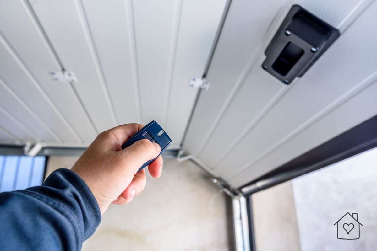 Hand aiming a garage door opener remote at the motor unit inside the garage