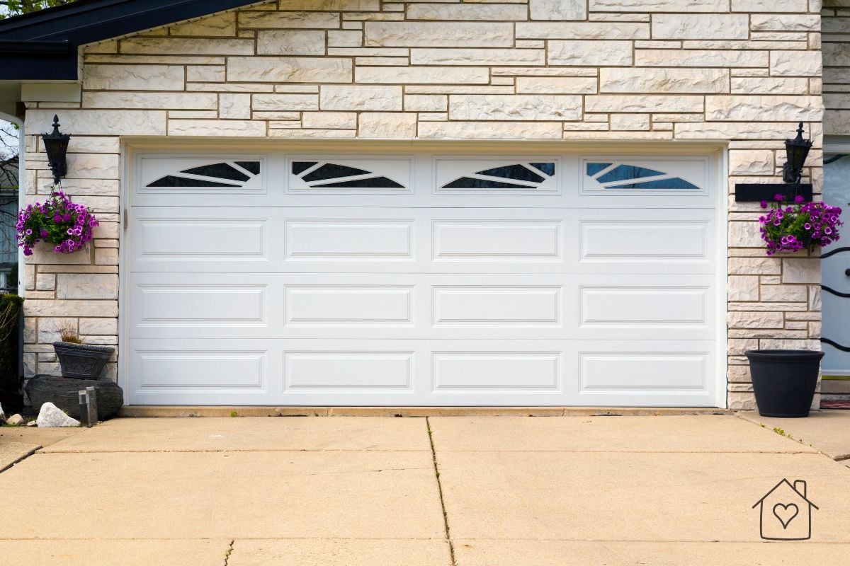 White residential garage door with arched window inserts on a stone home exterior