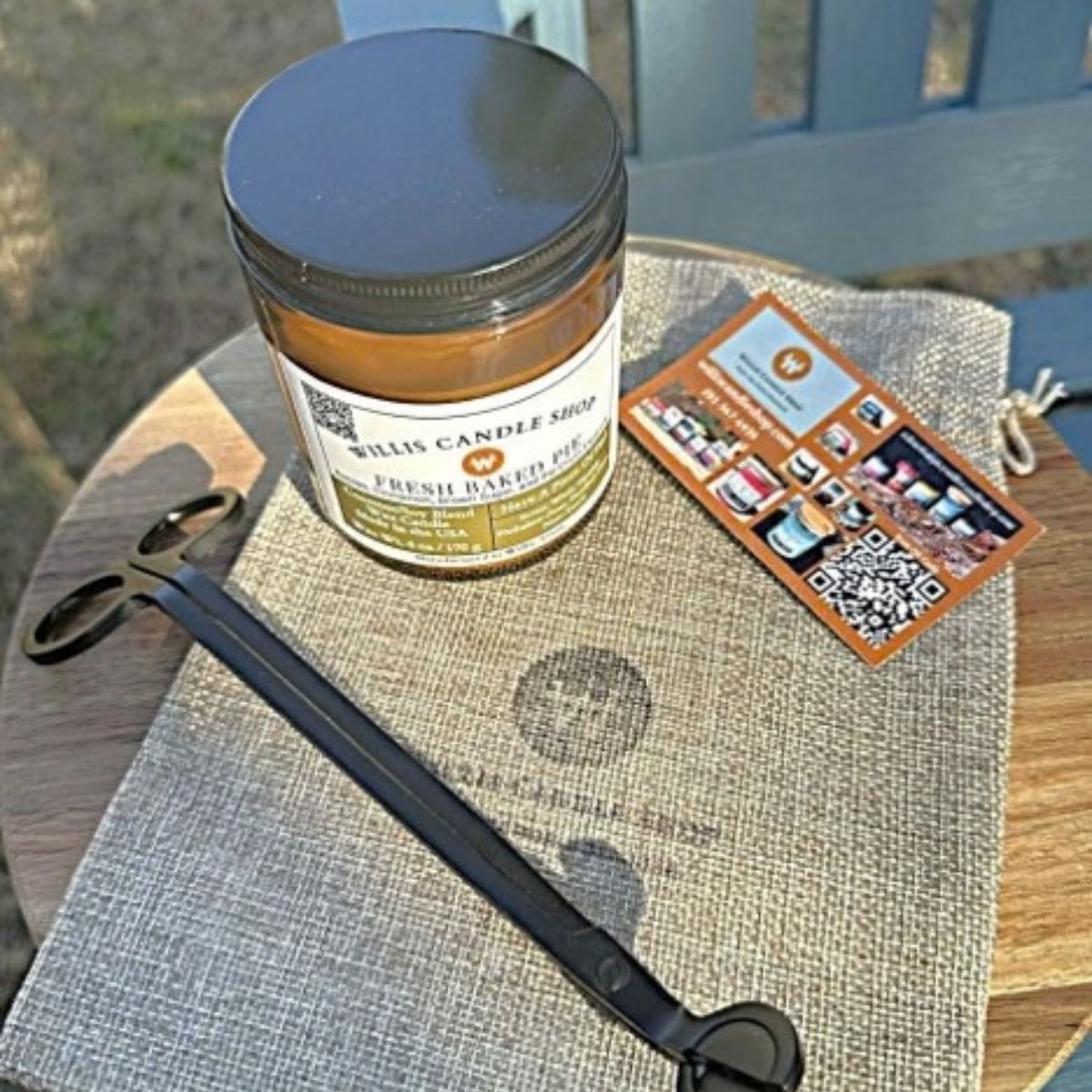 Amber glass Willis Candle Shop candle labeled Fresh Baked Pie, a coconut soy blend scented with cinnamon, brown sugar, and buttery crust, next to wick trimming scissors and a Willis Candle Shop info card