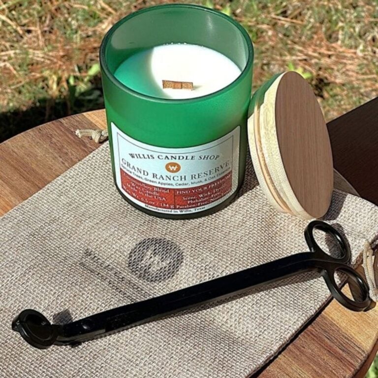 Green glass Willis Candle Shop candle labeled Grand Ranch Reserve, a coconut soy blend with spruce trees, green apples, cedar, musk, and oak essence, shown with a wood wick and trimming scissors