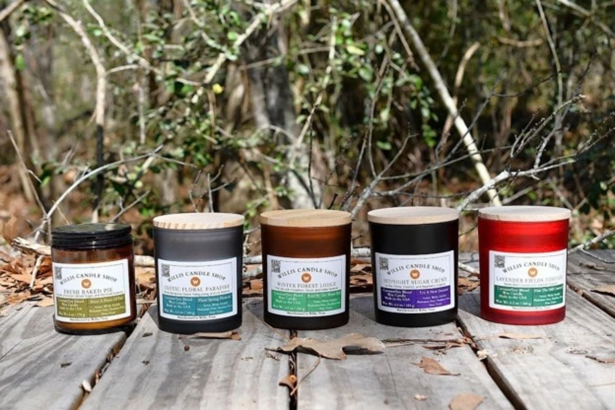 Five Willis Candle Shop coconut soy candles lined up outdoors, including Fresh Baked Pie, Exotic Floral Paradise, Winter Forest Lodge, Midnight Sugar Crisp, and Lavender Fields Forever, a mix of clean burning fall candles and year round scents