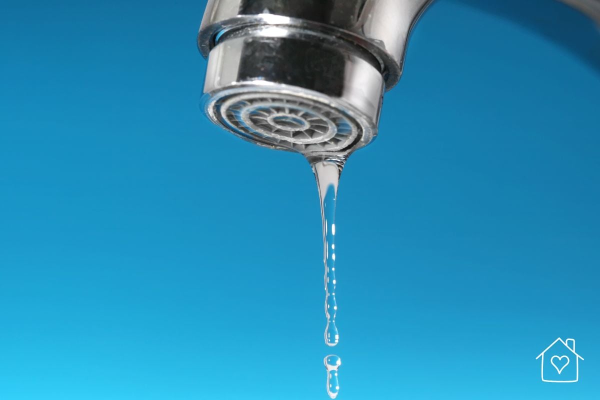 Close up of a chrome faucet with a thin stream of water dripping from it against a blue background