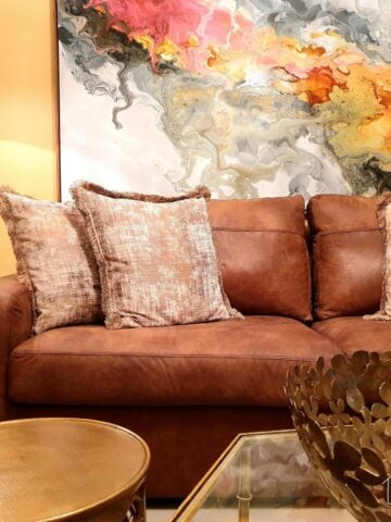 Cognac leather sofa with blush accent pillows styled against a colorful abstract art piece, part of a living room refresh