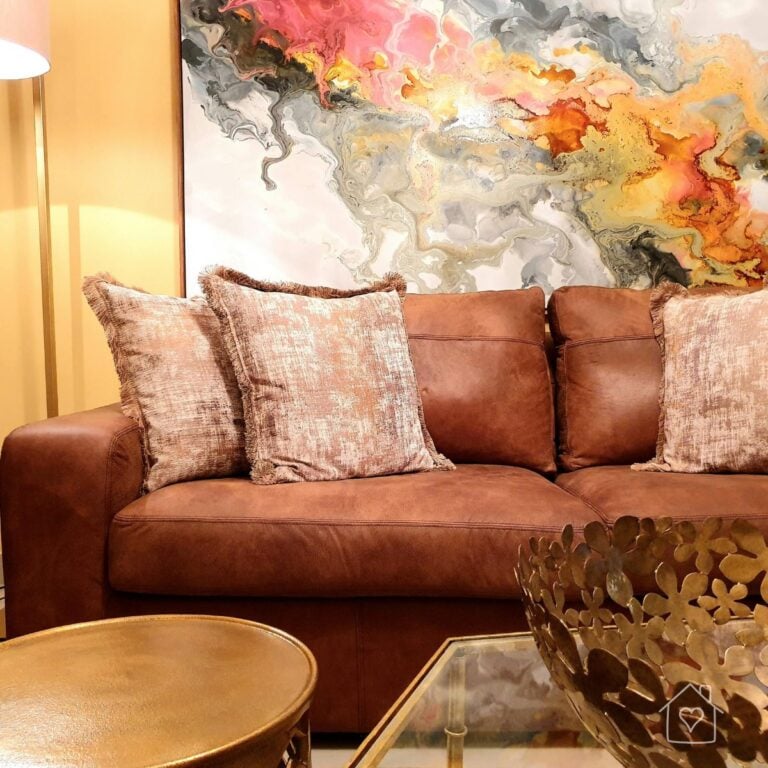 Cognac leather sofa with blush accent pillows styled against a colorful abstract art piece, part of a living room refresh