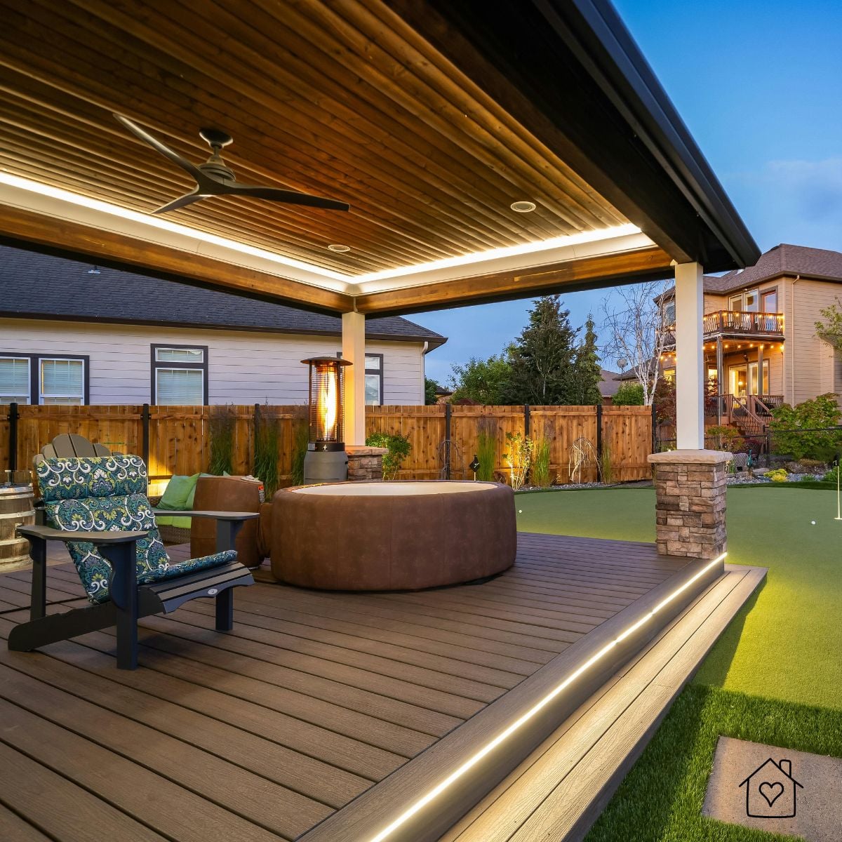 Covered patio with a wood plank ceiling, LED strip lighting and ceiling fan over a deck with a hot tub and patio heater