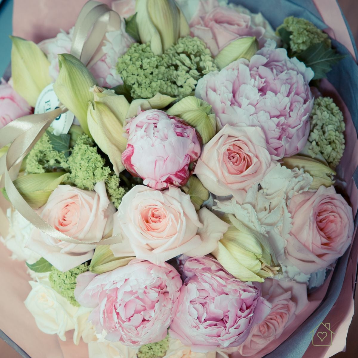 Round bouquet of pale pink peonies, blush roses, and green viburnum wrapped in pink and gray paper
