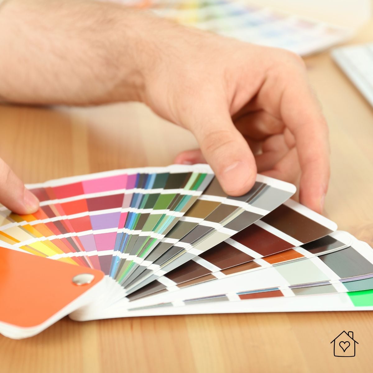 Hand holding a fan of colorful paint swatches to compare colors for a room makeover.
