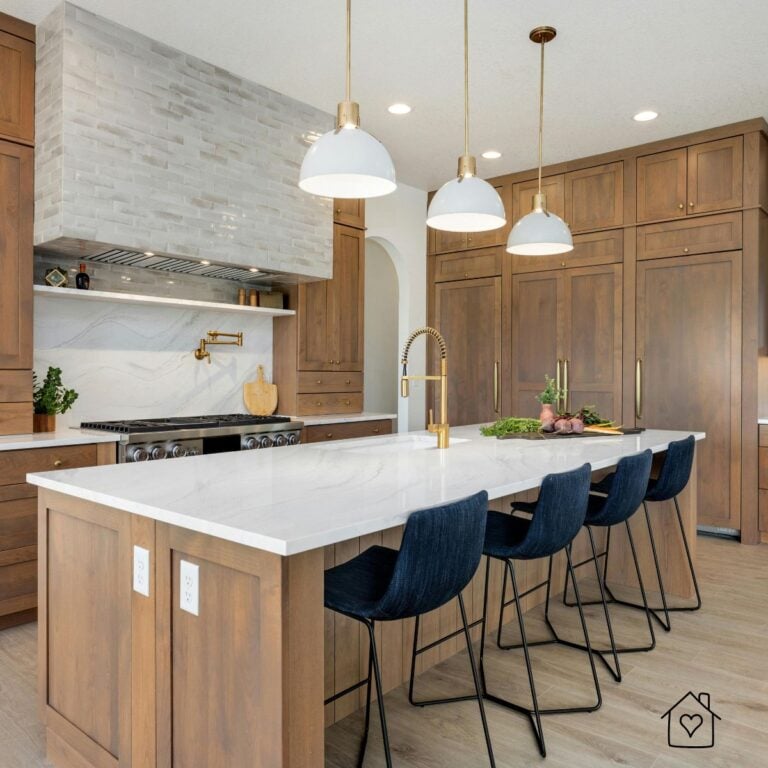 Kitchen with floor-to-ceiling stained wood shaker cabinets, a white quartz island, navy bar stools, and brass pendant lights