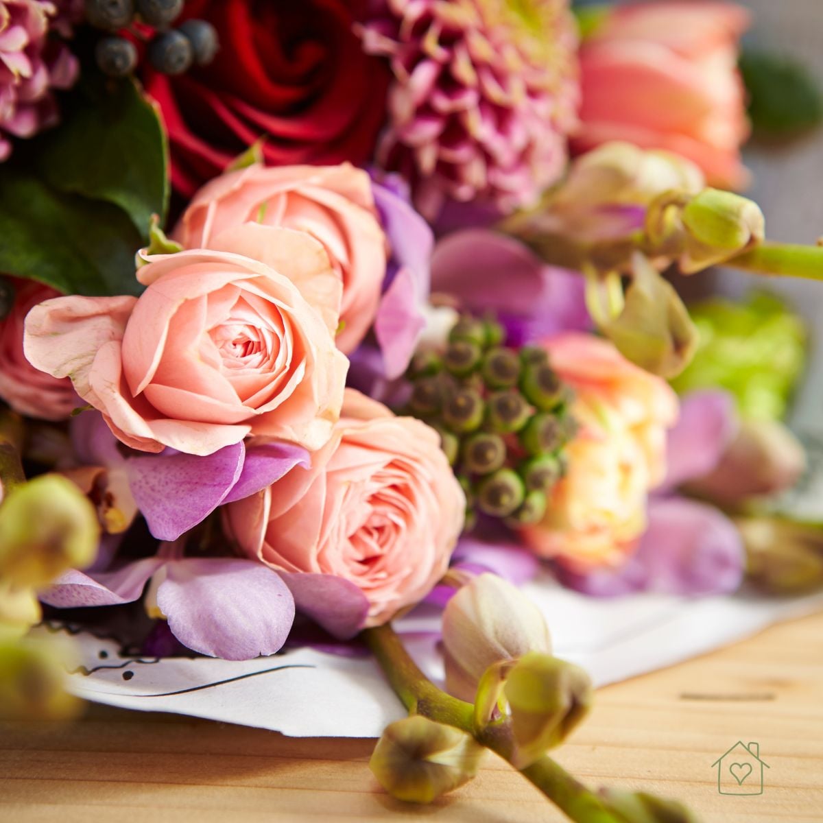 Close up of peach spray roses, lavender orchids, and a purple dahlia in a bouquet on a wooden table