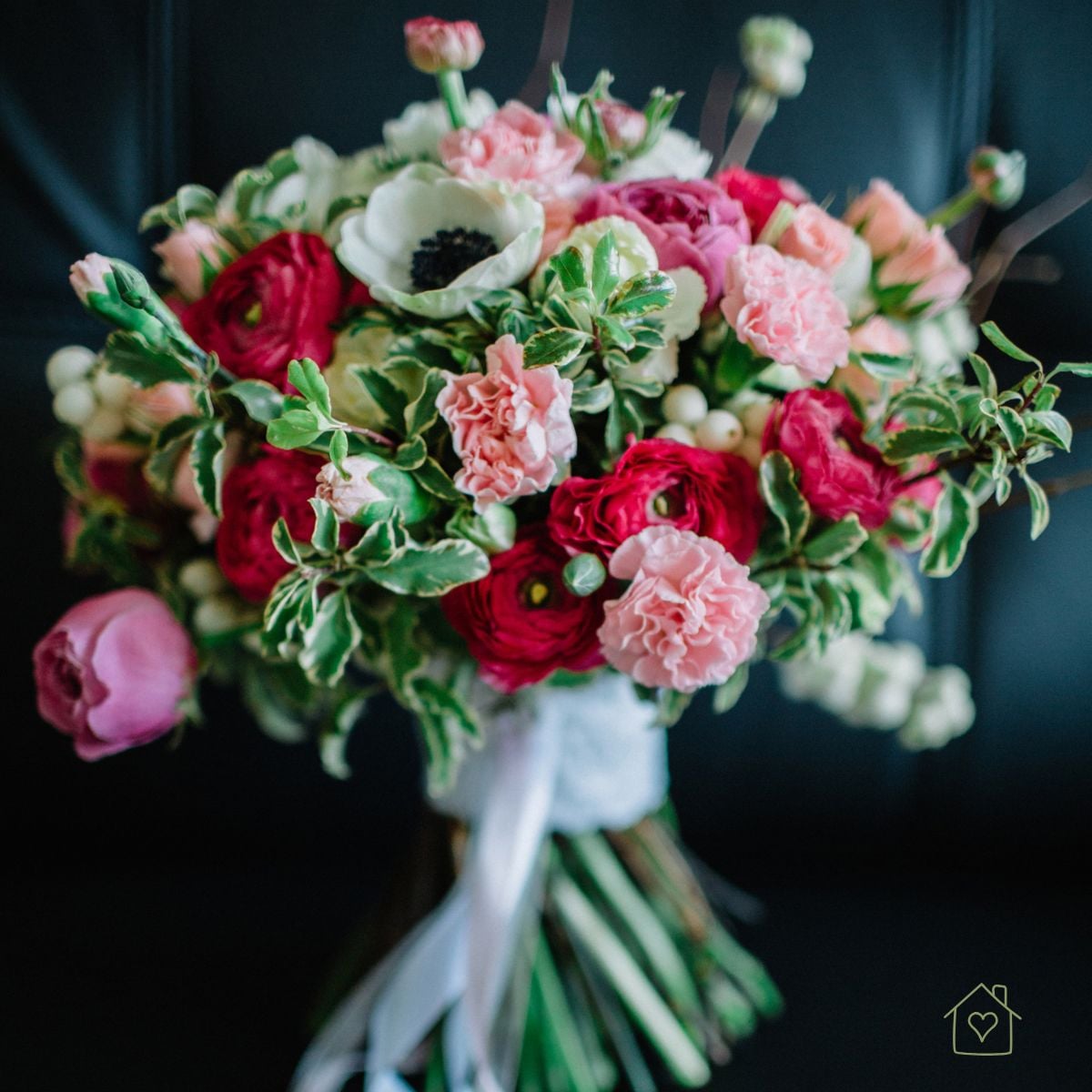 Hand-tied bouquet of red ranunculus, a white anemone, and pink carnations with white ribbon