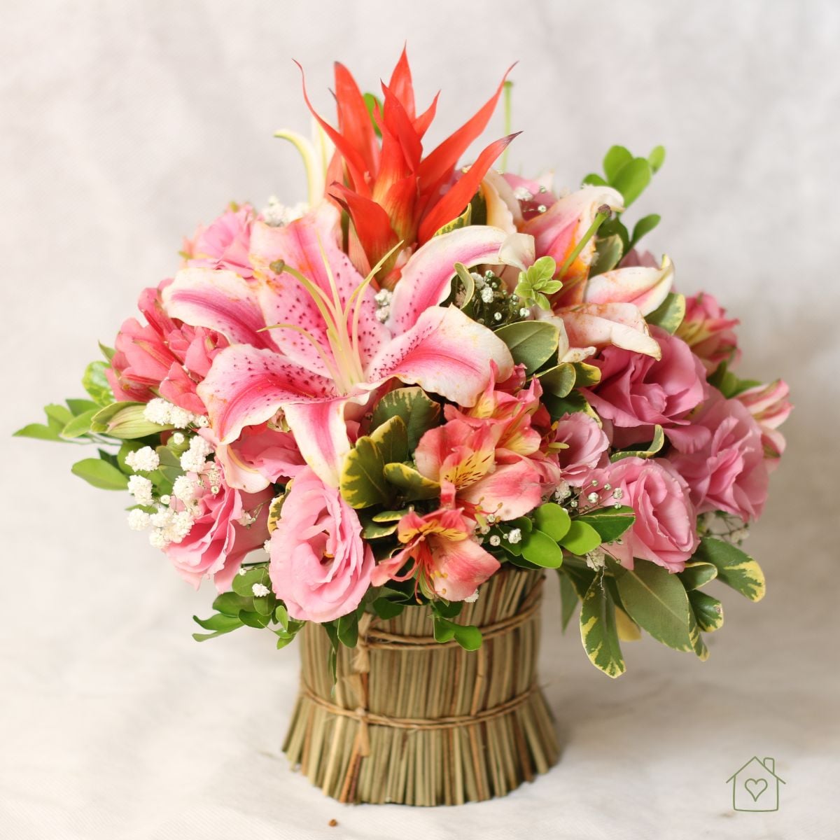 Low arrangement of pink stargazer lilies, lisianthus, and alstroemeria in a straw-wrapped vase