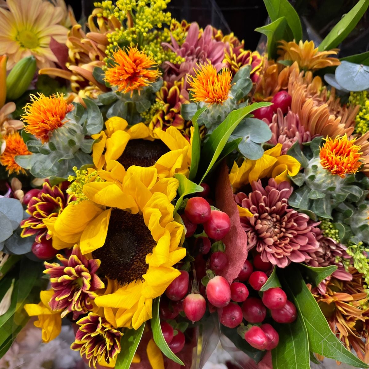 Fall bouquet of yellow sunflowers, orange safflowers, rust colored mums, and red hypericum berries