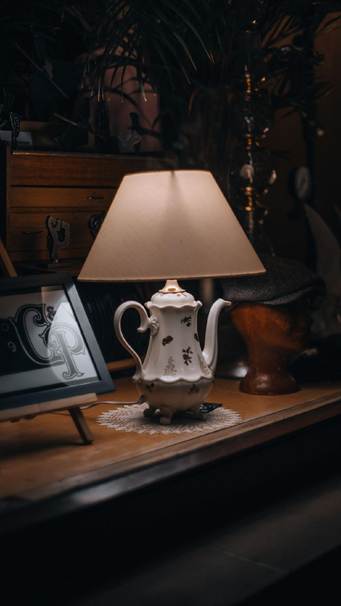 Teapot-style ceramic table lamp with a tan shade on a dark wooden side table