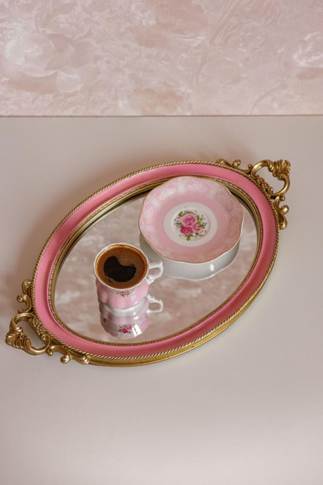 Pink and gold oval mirrored tray with ornate handles holding a floral saucer and espresso cup