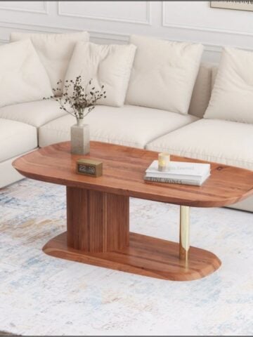 Oval wooden coffee table with a fluted pedestal base and brass leg in front of a cream sectional sofa